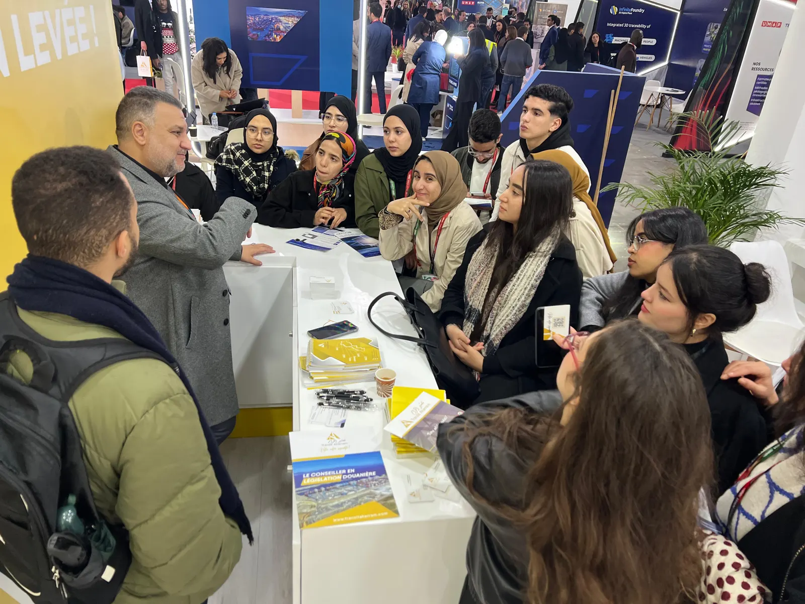 Étudiants écoutant un conseiller en législation douanière sur un stand du salon WAM